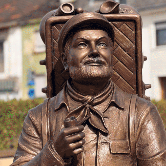 Bronzefigur Mann mit Rucksack sitzend