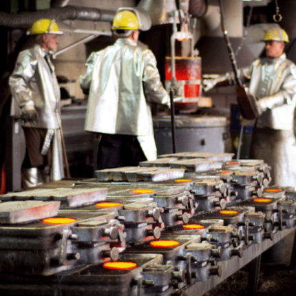 Drei Arbeiter in Sicherheitskleidung giessen Metal
