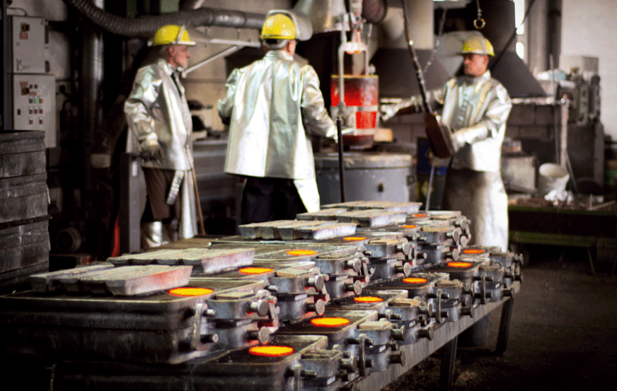Drei Arbeiter in Sicherheitskleidung giessen Metal